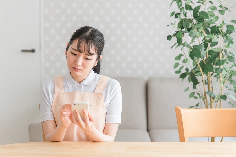 エプロン姿の女性がスマホを見て悩む